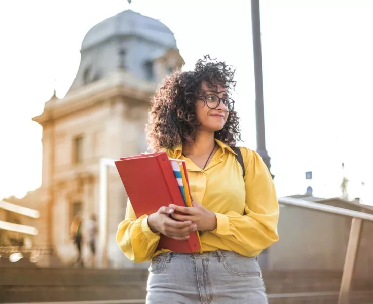 etudiante devant un batiment, tient un porte document