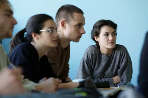 étudiants du campus de Lyon. 3 étudiants en salle de classe sont de profil, une étudiante face appareil regarde le professeur