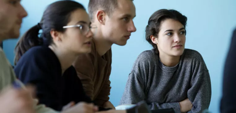 étudiants du campus de Lyon. 3 étudiants en salle de classe sont de profil, une étudiante face appareil regarde le professeur