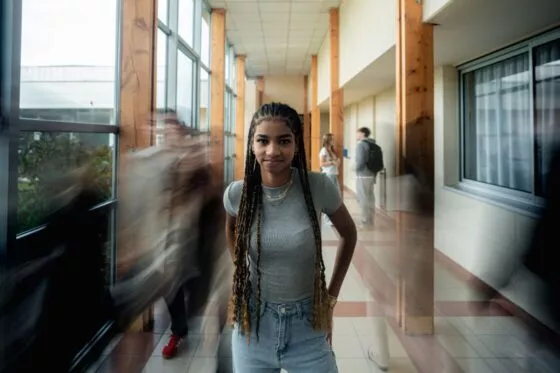 étudiante regarde droit vers l'appareil dans un couloir où les autres passent vite et sous un peu flous