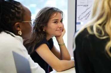 etudiante du campus de l'ESSCA à Bordeaux assise en classe à un bureau, regarde ses camarades avec la tête appuyée sur la main