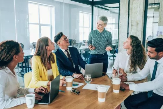 reunion avec plusieurs personnes autour d'une table de réunion. une femme est debout et s'exprime