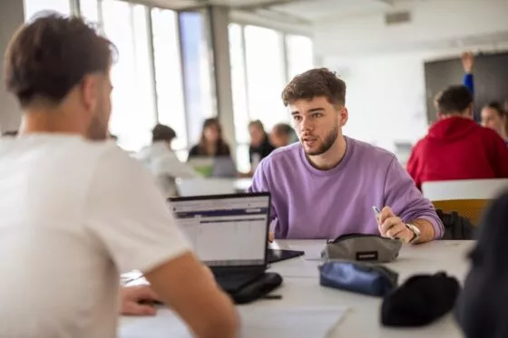 deux étudiants du campus de l'ESSCA à Bordeaux, discutent face à face. Ils sont assis dans une salle de classe