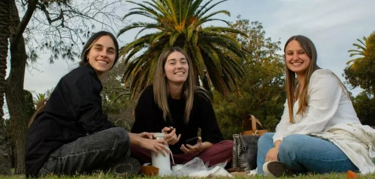 3 étudiantes souriantes, assises dans l'herbes