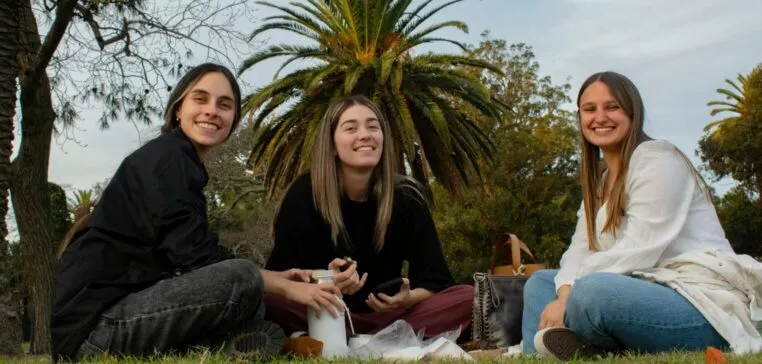 3 étudiantes souriantes, assises dans l'herbes